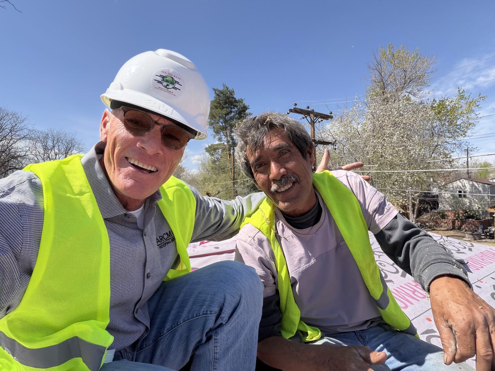 Two ARCM Roofing team members in safety vests on a roof with new underlayment