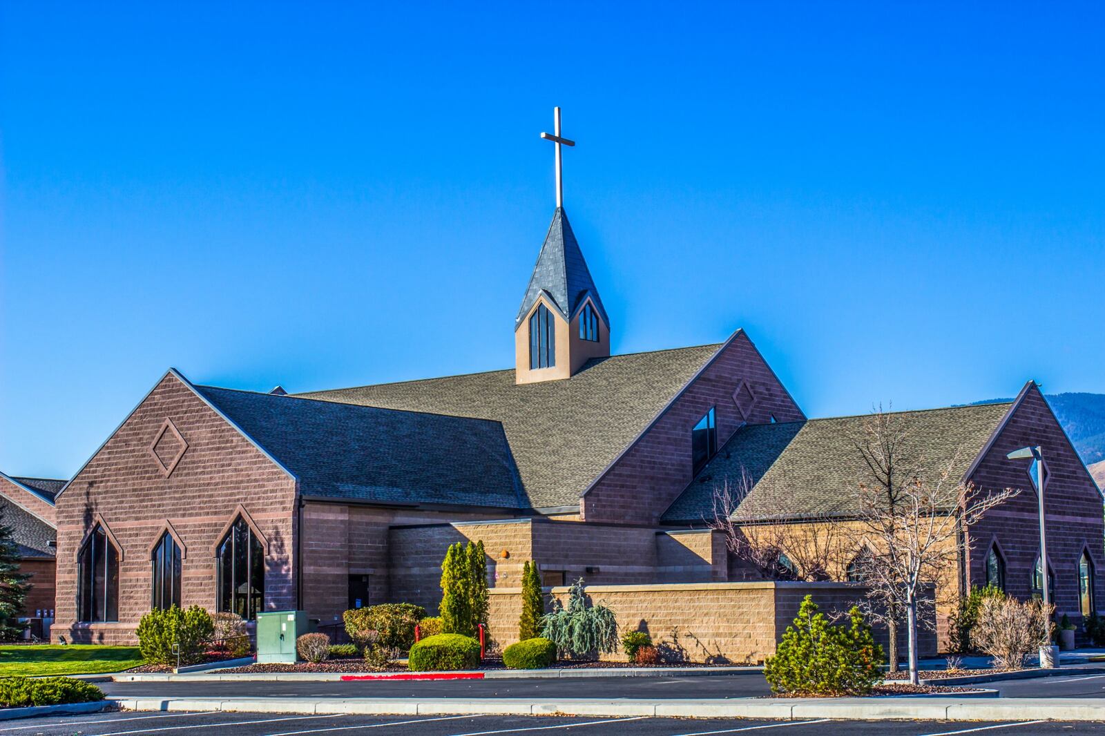 Brick church with steep gabled shingle roofs and a slate-clad bell tower with a cross